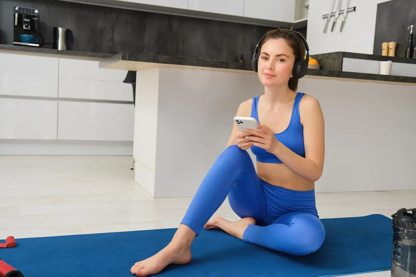 Porträt einer jungen, glücklichen Frau, die mit Kopfhörern trainiert und Musik hört, während sie im Sitzen Yoga macht.